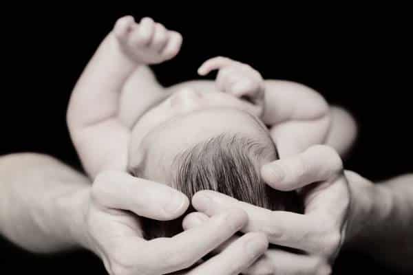 Photo de mains autour de la tête d'un bébé pour illustrer l'ostéopathie comme moyen de prévenir la plagiocéphalie.